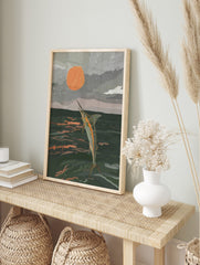 Illustrative print of a marlin leaping from dark ocean water towards a large orange sun in a, in an alternate framed mockup