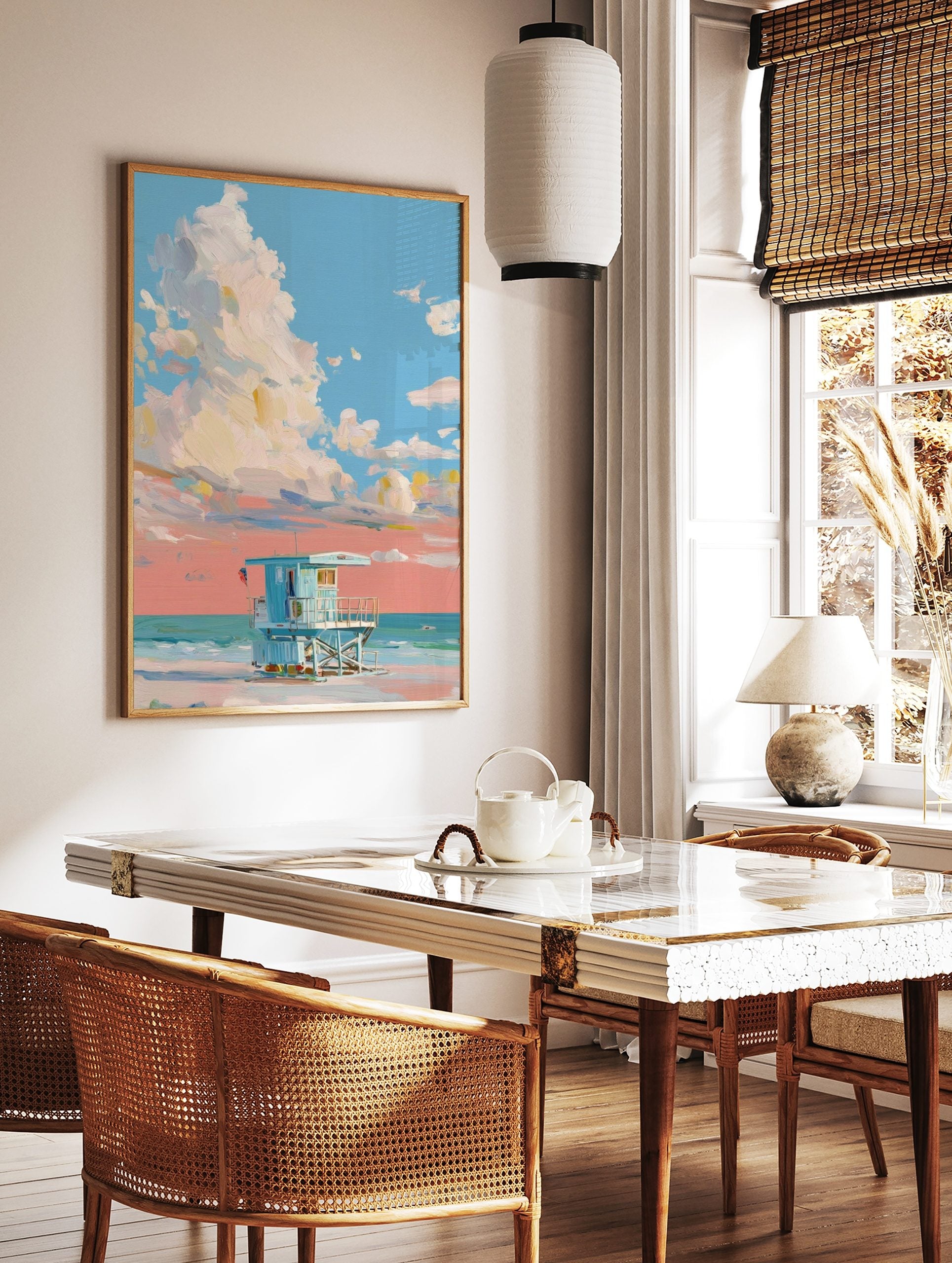 Painterly art print of a light blue lifeguard hut on a beach under a sky with large white and peach, in a styled room mockup