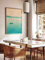 Minimalist teal landscape print with a lone boatman on a lake and distant mountains under a pale sky, in a styled room mockup