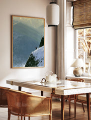 Lone skier in an orange jacket on a steep, snow-covered mountain ridge with layered peaks in the, in a styled room mockup