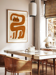 Minimalist wall art print featuring an elongated orange cat illustration with black facial features, in a styled room mockup