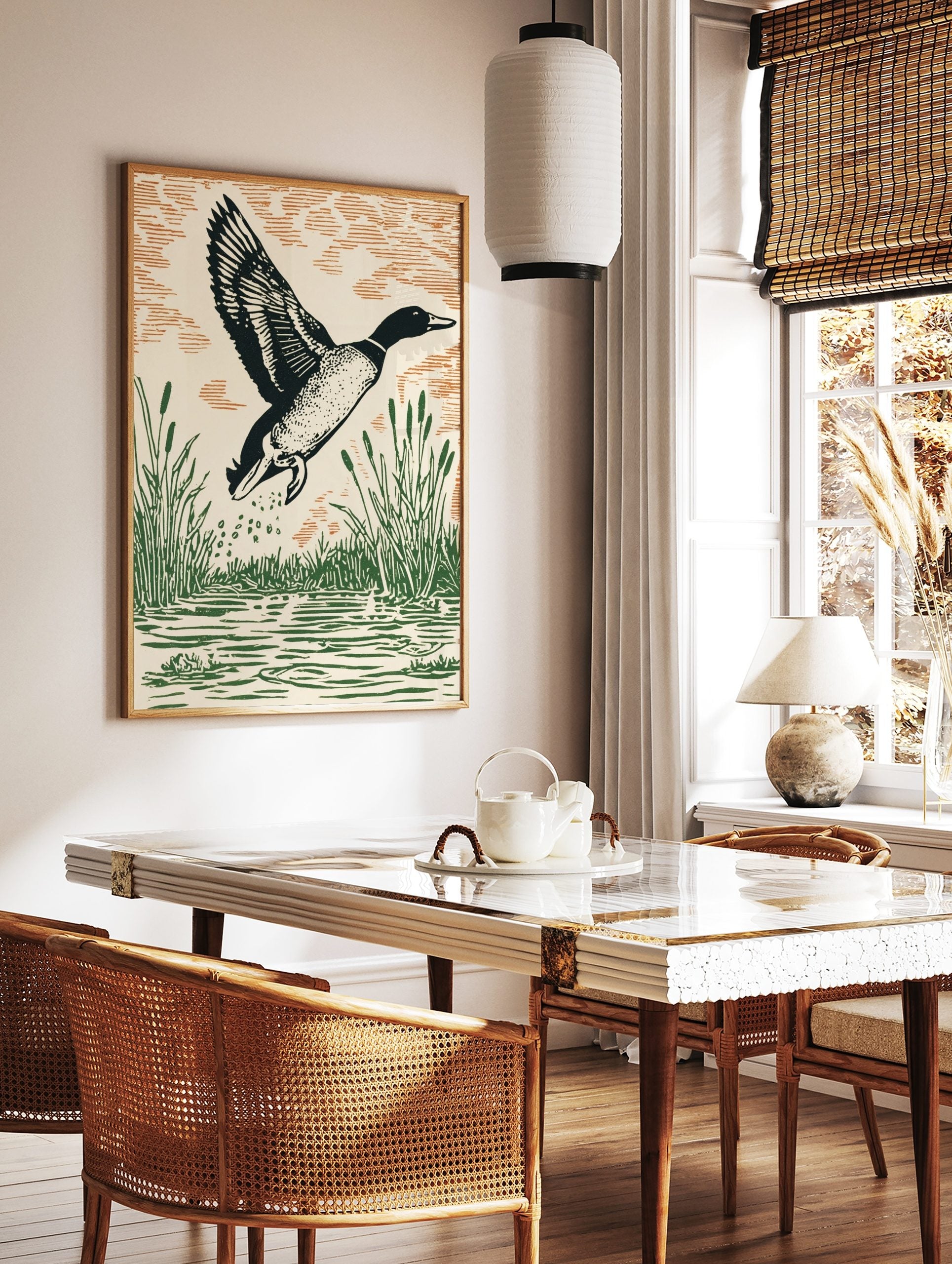 Linocut style art print of a mallard duck flying from water with green reeds and orange-brown sky, in a styled room mockup
