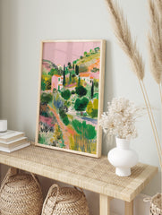 Illustrative Mediterranean landscape print with pink houses, green hills, cypress trees, and, in an alternate framed mockup