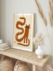 Minimalist brown cat illustration with long serpentine tail and red seal mark on cream, in an alternate framed mockup