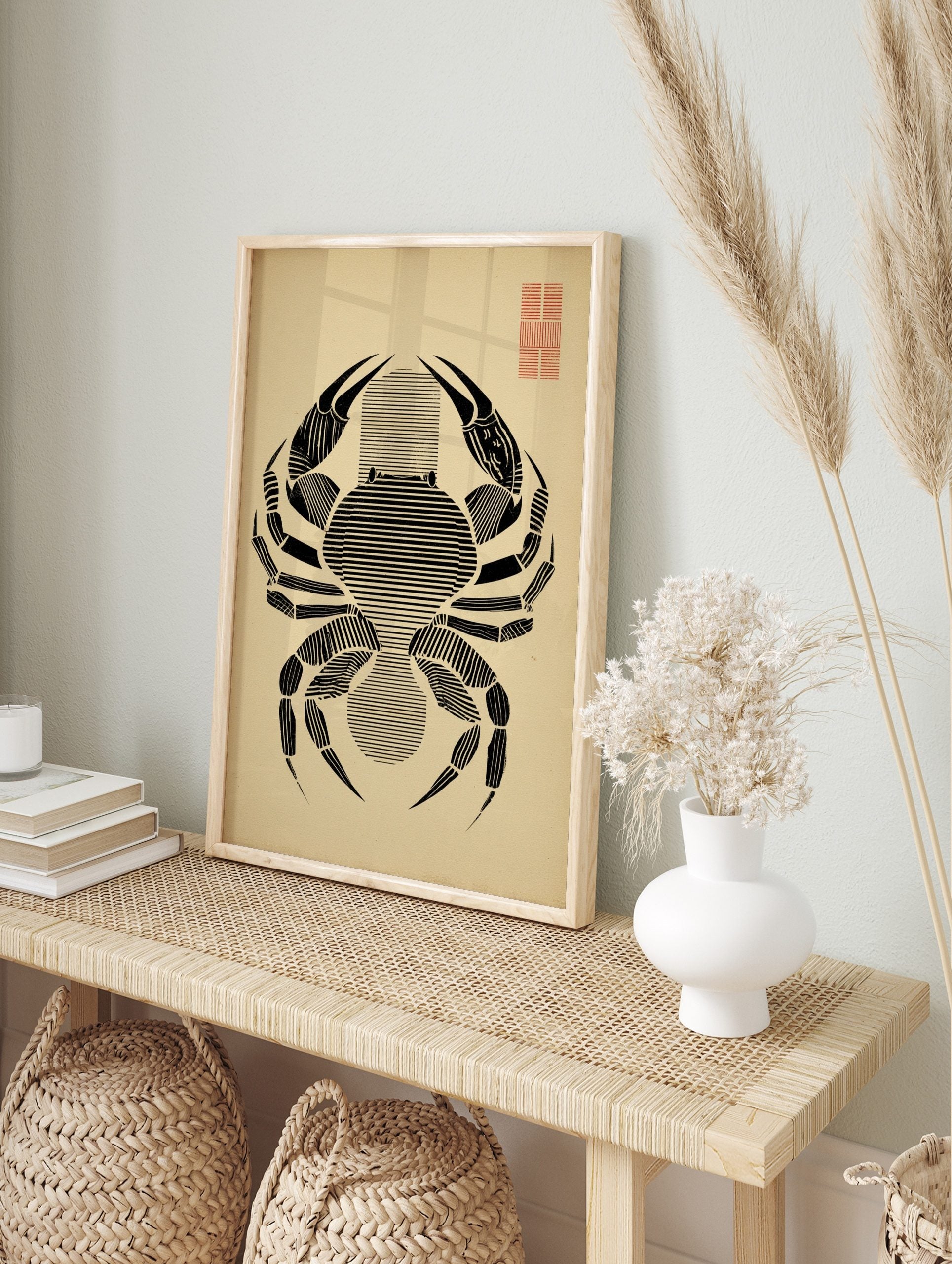 Minimalist black crab illustration with horizontal lines on beige paper, red grid in top right, in an alternate framed mockup