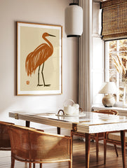 Minimalist crane bird illustration in burnt orange with dark legs on a cream background, in a styled room mockup