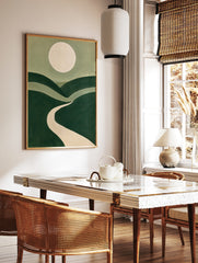 Minimalist landscape art print with rolling green hills, a winding beige path, and a large pale, in a styled room mockup