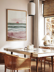 Minimalist watercolour art print of a sunset over the ocean with red sun, green-blue waves, and, in a styled room mockup