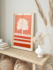 Minimalist tree silhouette art print with horizontal stripes in warm coral and peach tones on, in an alternate framed mockup