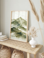 Watercolour painting of a layered misty mountain range with snow-capped peaks in green and, in an alternate framed mockup