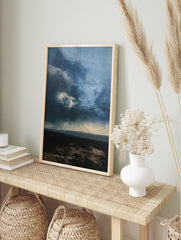 Moody, dark stormy landscape with heavy clouds and a textured horizon line in shades of blue, in an alternate framed mockup