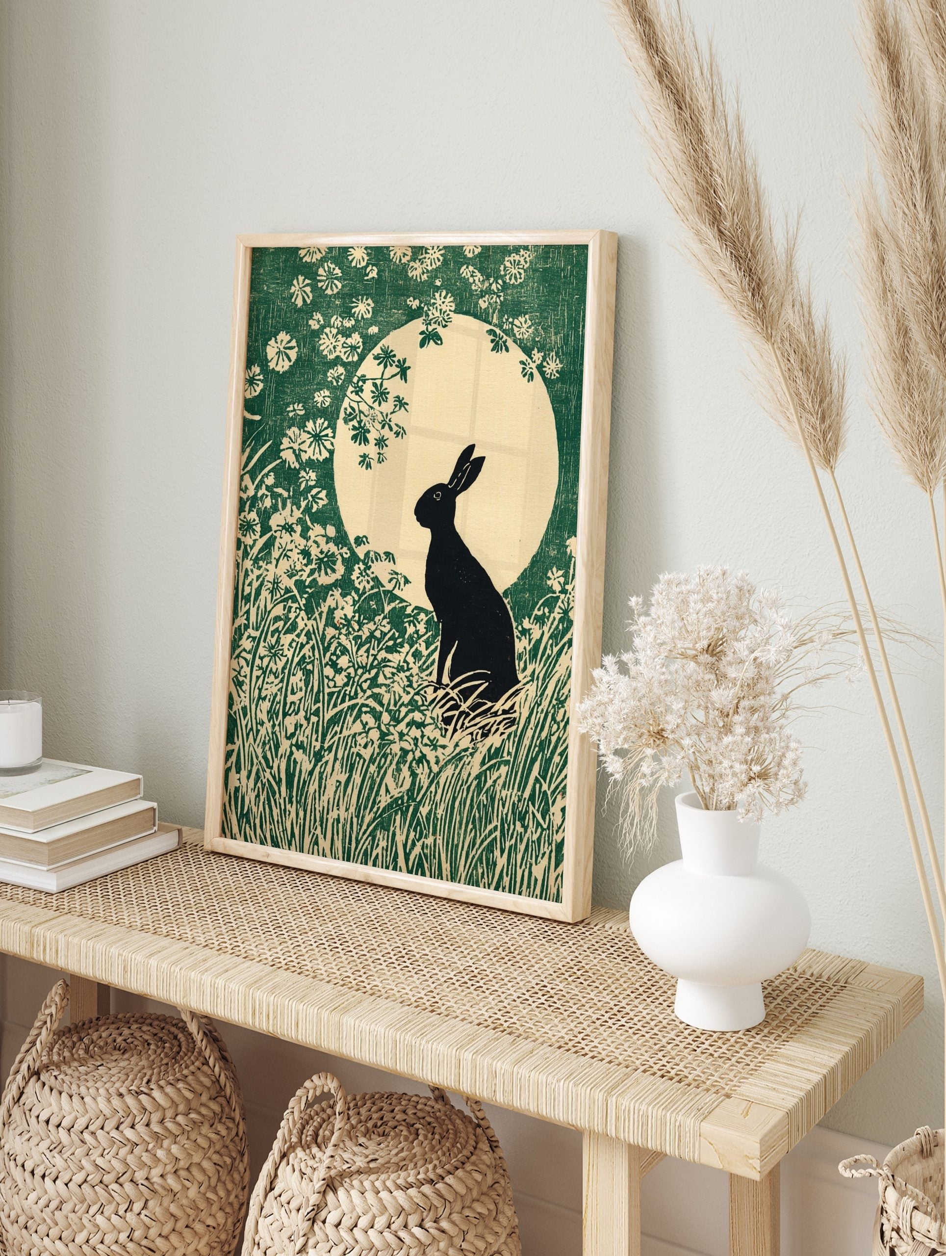 Black rabbit silhouette in a field of green grass and white flowers against a large pale moon, in an alternate framed mockup