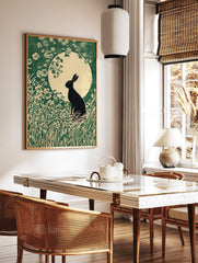 Black rabbit silhouette in a field of green grass and white flowers against a large pale moon in an, in a styled room mockup