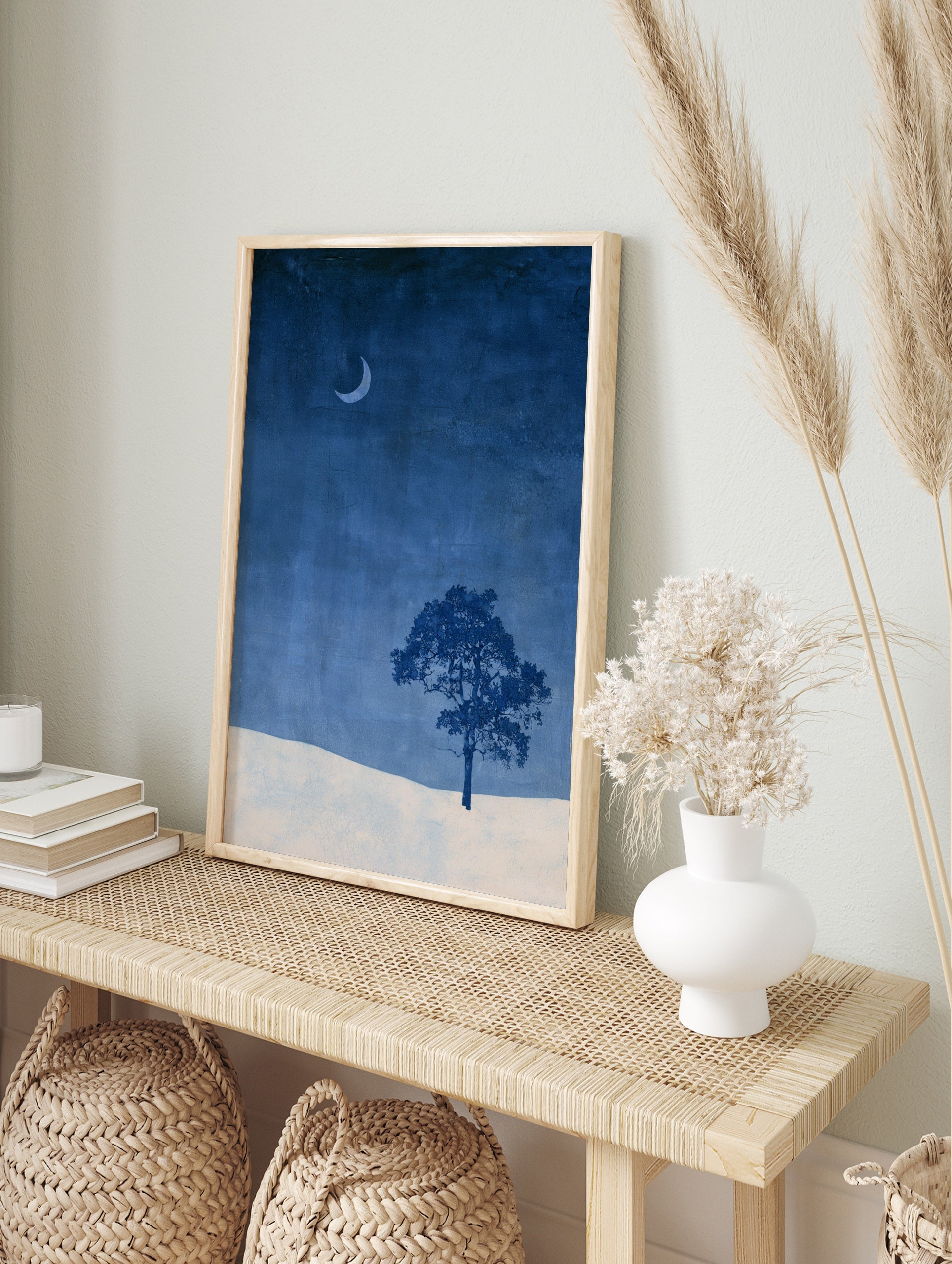 Minimalist wall art print of a single tree and crescent moon over a snowy landscape in deep, in an alternate framed mockup