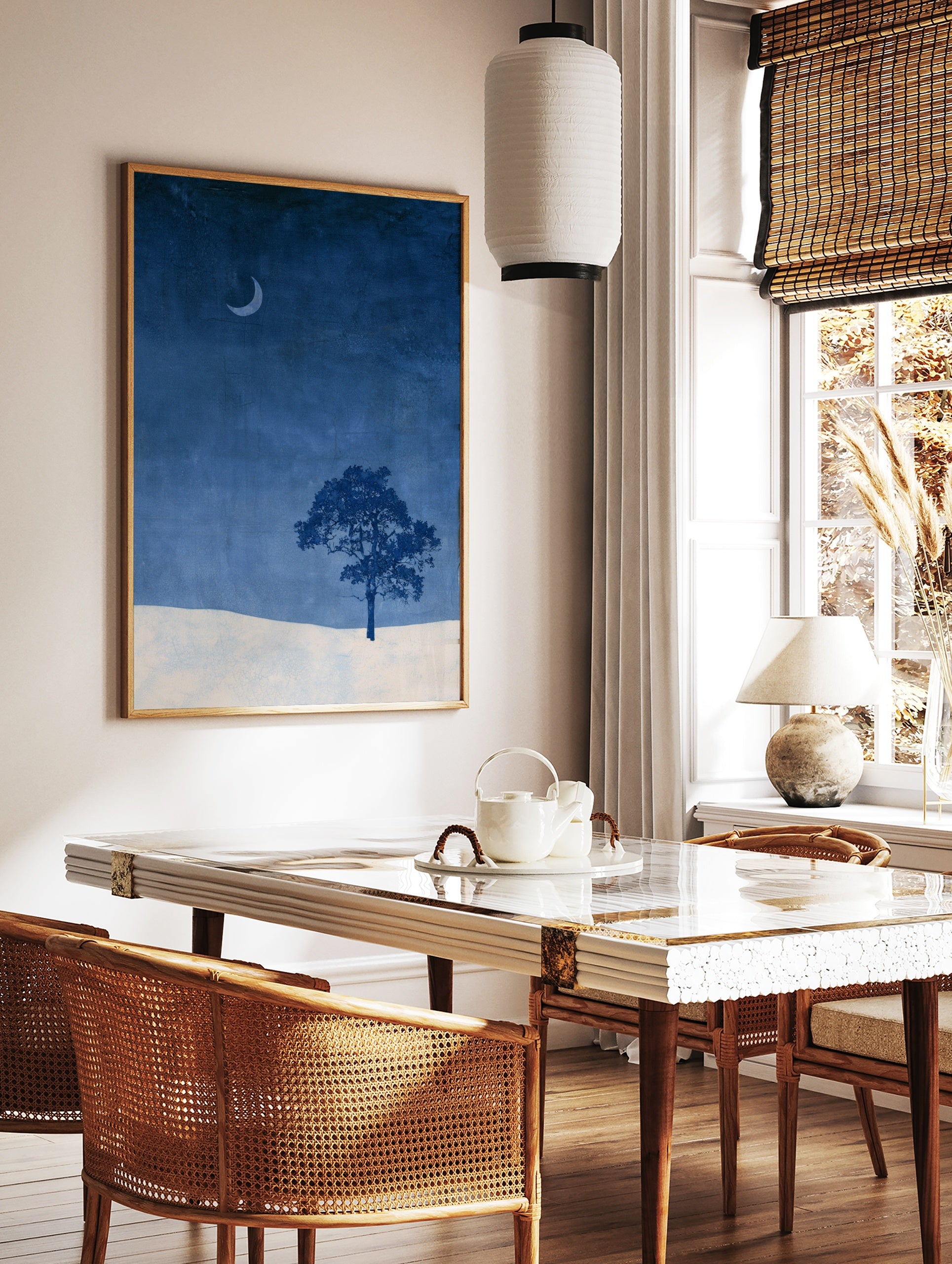 Minimalist wall art print of a single tree and crescent moon over a snowy landscape in deep blue, in a styled room mockup