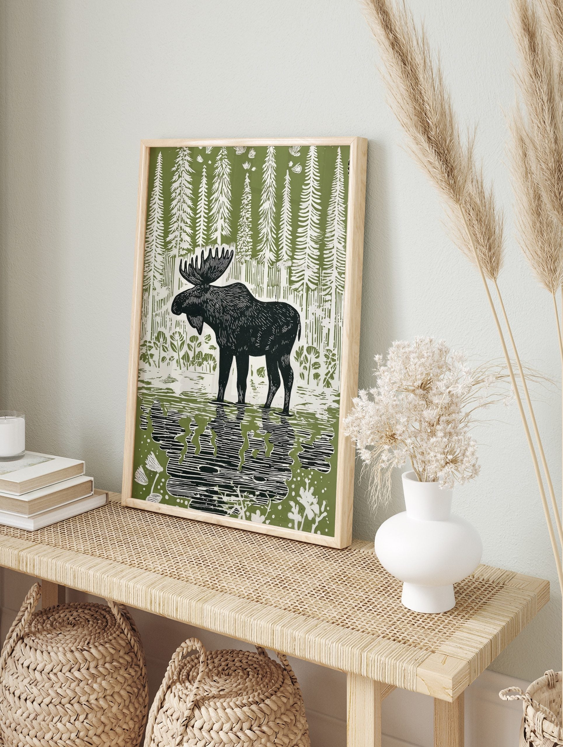 Linocut style print of a black moose standing in water with reflections, surrounded by white, in an alternate framed mockup