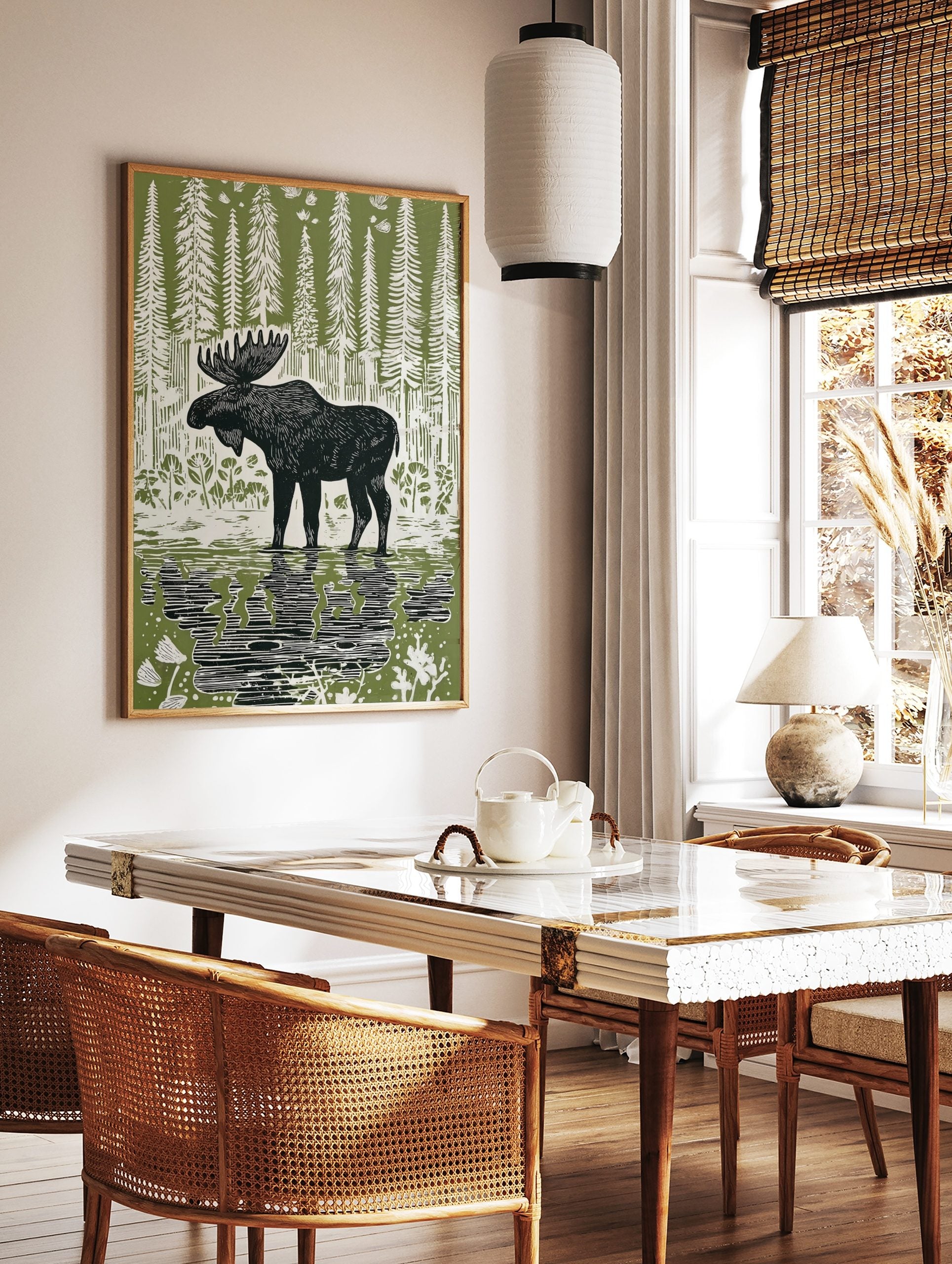 Linocut style print of a black moose standing in water with reflections, surrounded by white trees, in a styled room mockup
