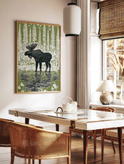 Linocut style print of a black moose standing in water with reflections, surrounded by white trees, in a styled room mockup
