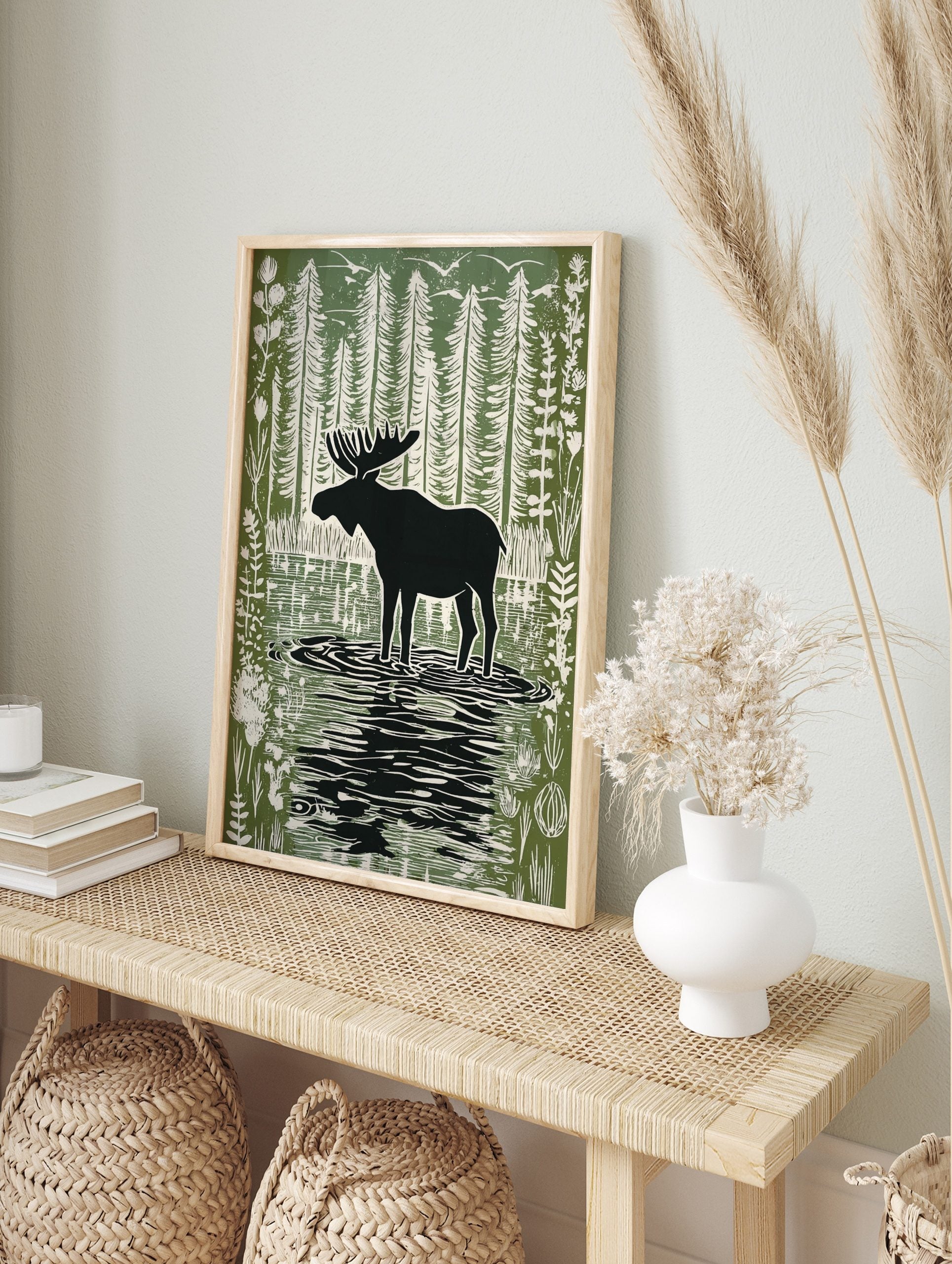 Moose silhouette standing in a forest lake with tall trees and birds in a green and white, in an alternate framed mockup