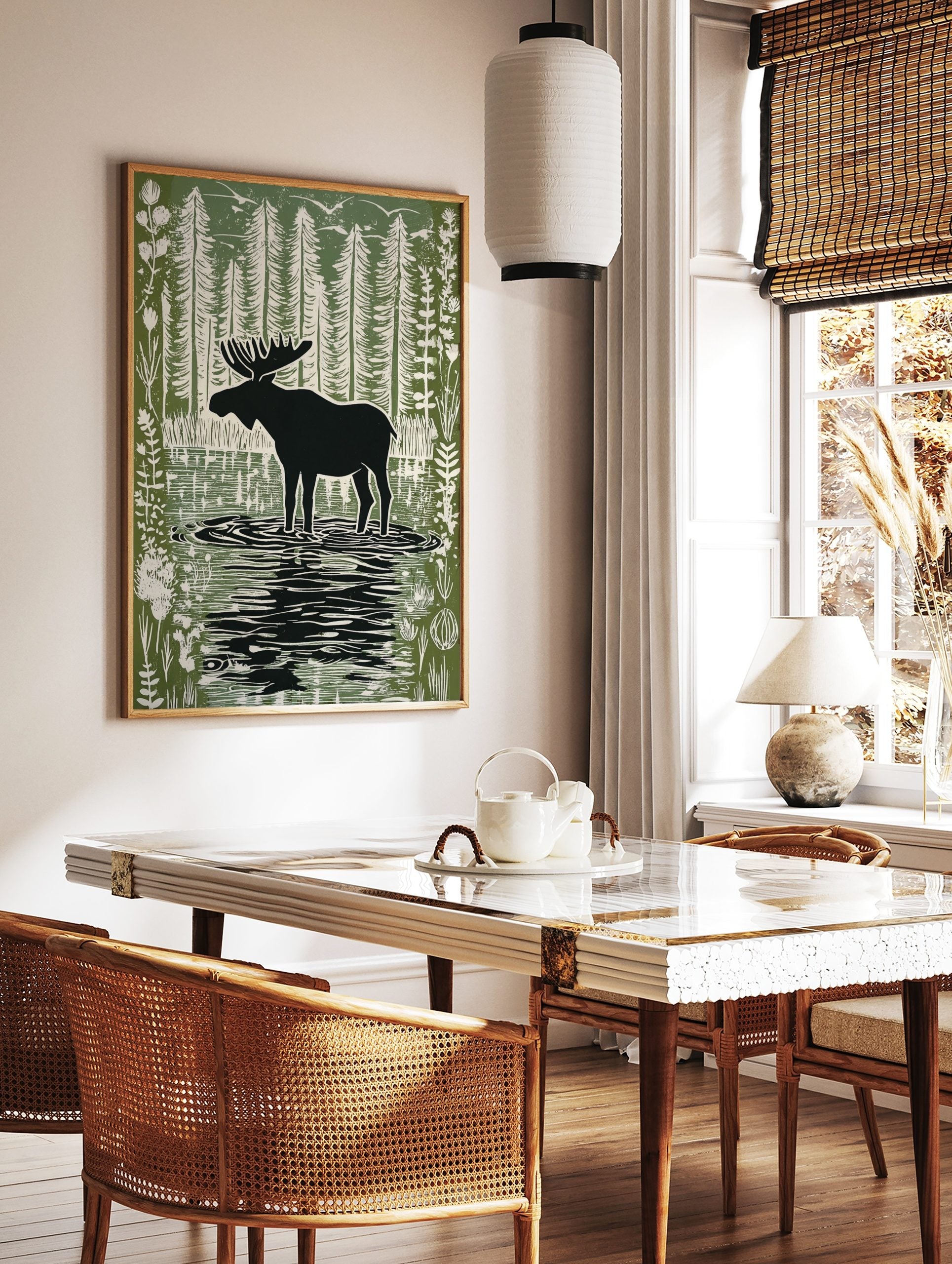 Moose silhouette standing in a forest lake with tall trees and birds in a green and white linocut, in a styled room mockup