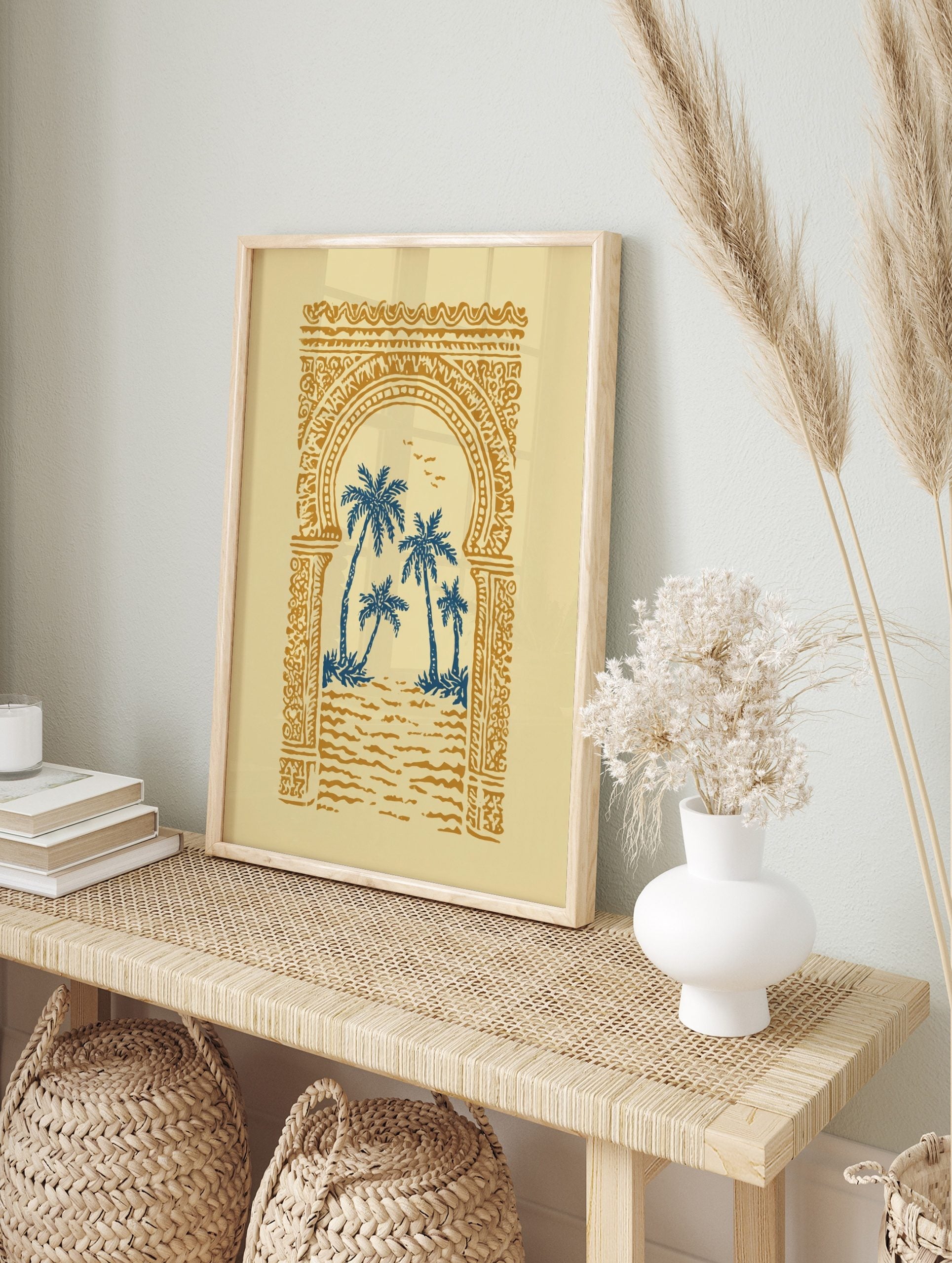 Illustrative print of blue palm trees through an ornate golden Moroccan archway on a cream, in an alternate framed mockup