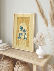 Illustrative print of blue palm trees through an ornate golden Moroccan archway on a cream, in an alternate framed mockup