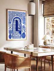 Blue and white illustrative art print of a Moroccan arched doorway with open door, botanical, in a styled room mockup
