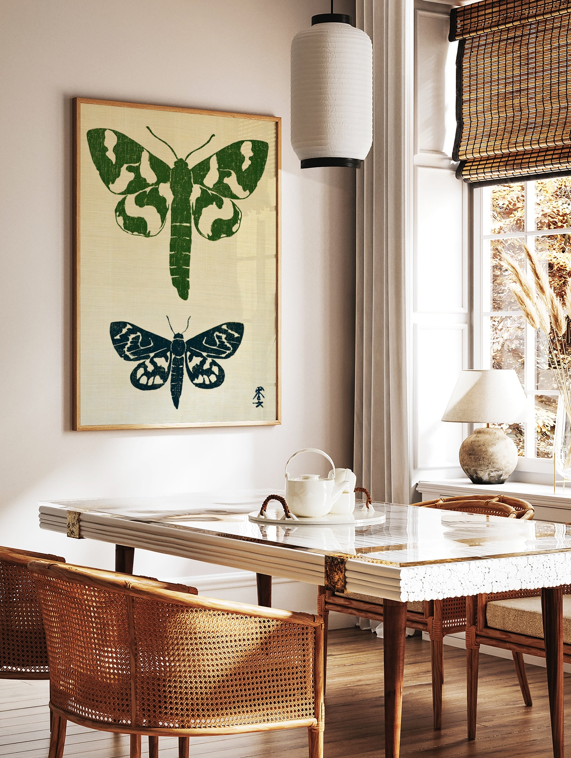 Two moth illustrations in green and navy block-print style on a textured neutral background, in a styled room mockup