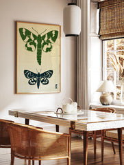 Two moth illustrations in green and navy block-print style on a textured neutral background, in a styled room mockup