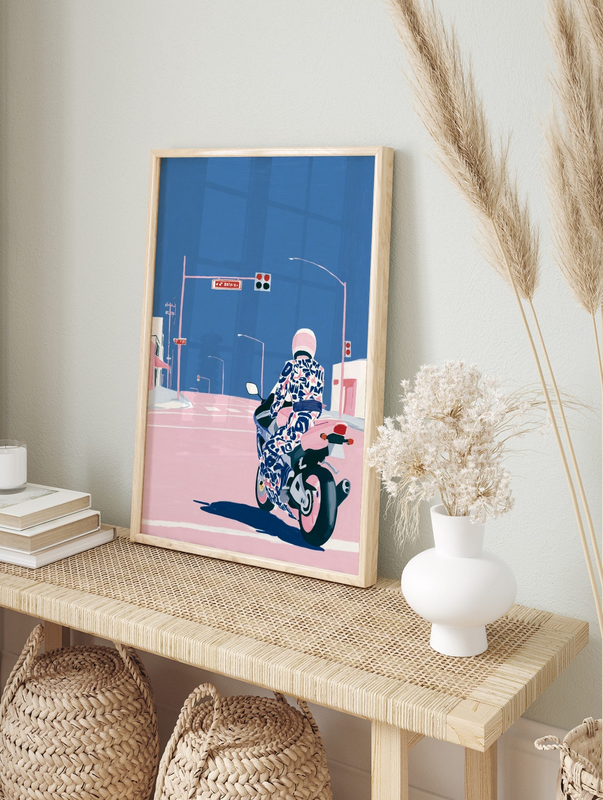 Illustrative motorcycle wall art with rider in patterned suit and pink helmet at city, in an alternate framed mockup