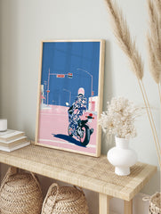 Illustrative motorcycle wall art with rider in patterned suit and pink helmet at city, in an alternate framed mockup