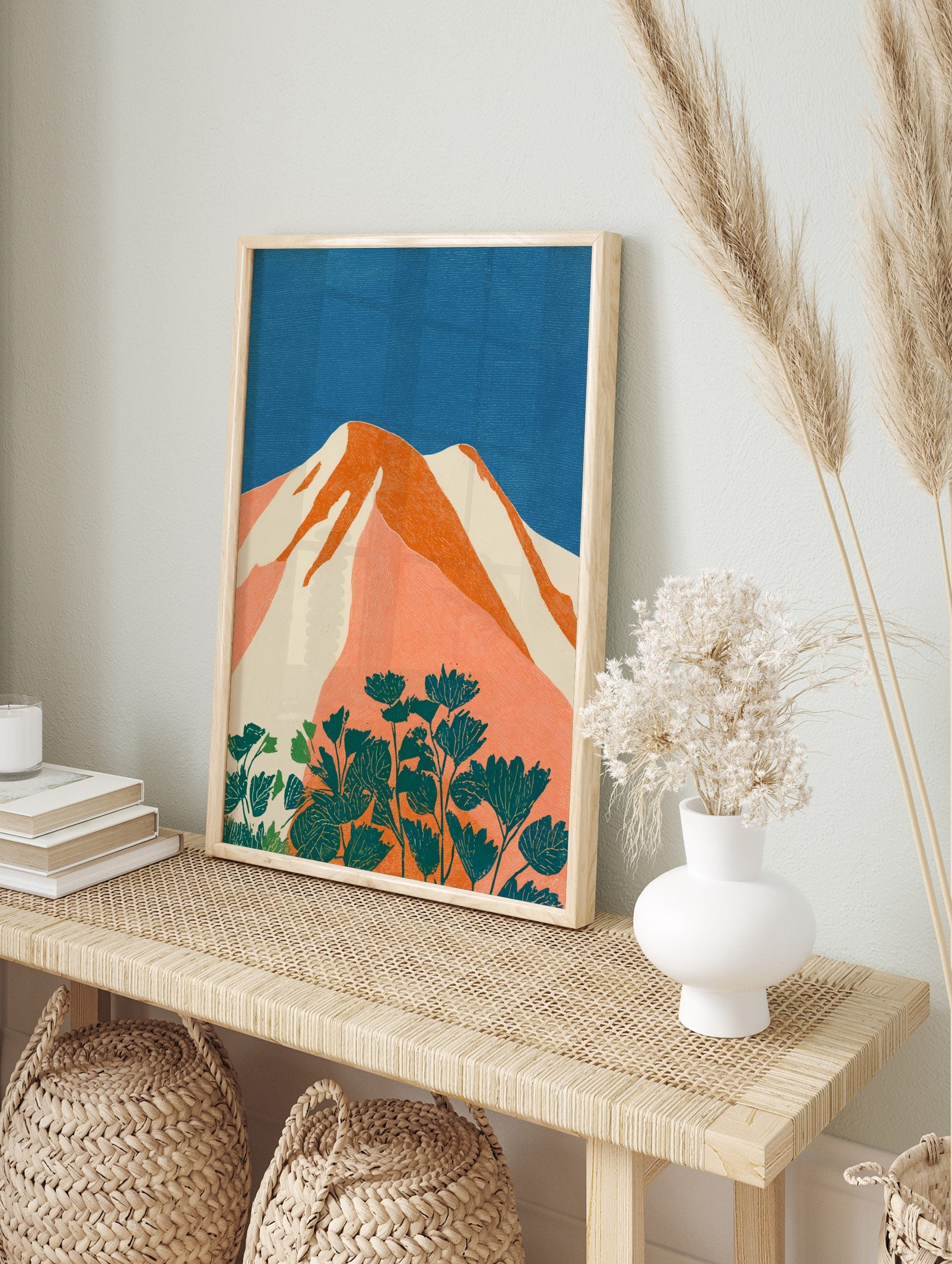 Stylised mountain landscape art print with orange peaks, white snow, blue sky, and teal, in an alternate framed mockup