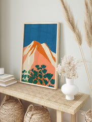 Stylised mountain landscape art print with orange peaks, white snow, blue sky, and teal, in an alternate framed mockup