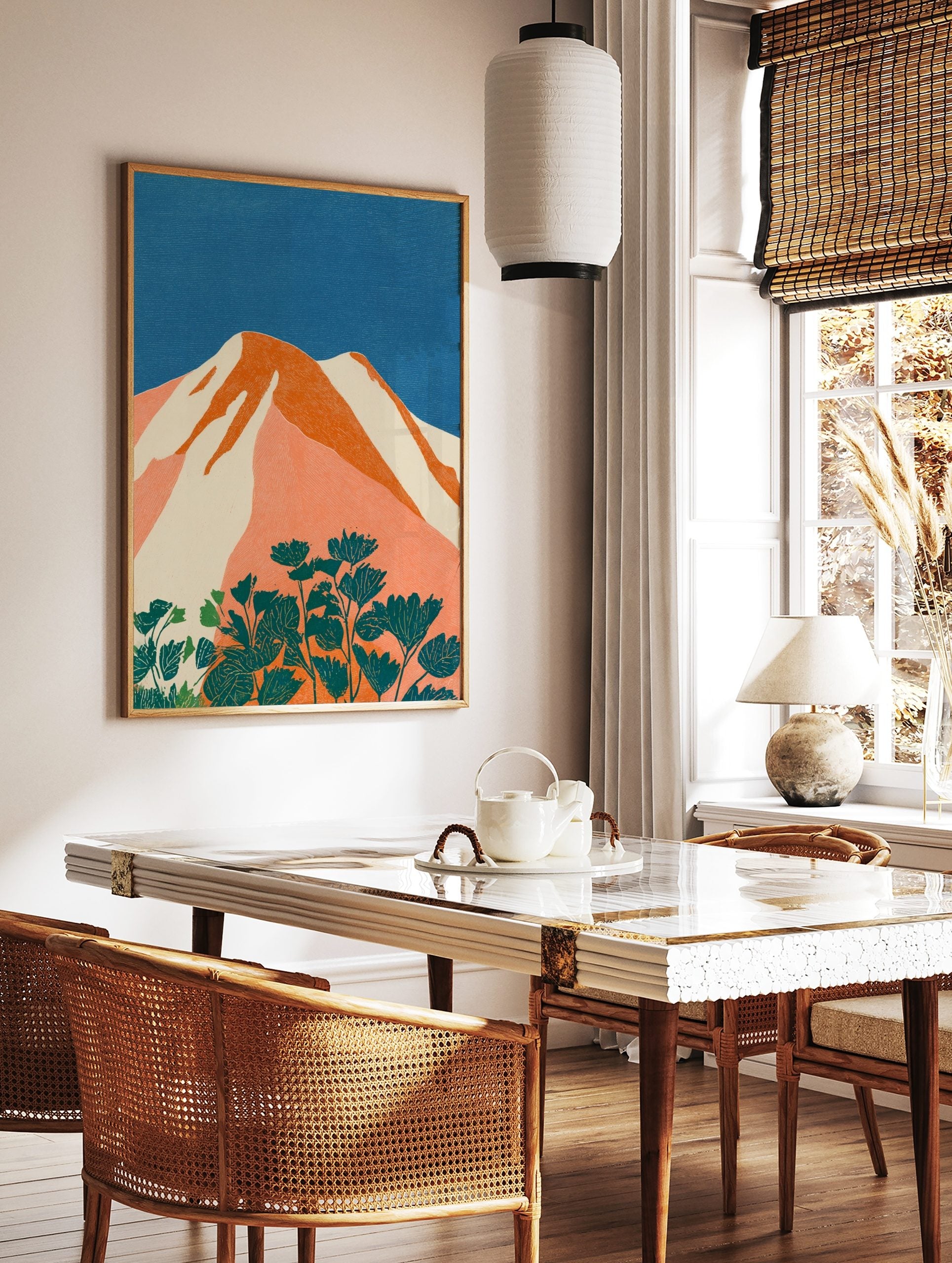 Stylised mountain landscape art print with orange peaks, white snow, blue sky, and teal flowers, in a styled room mockup