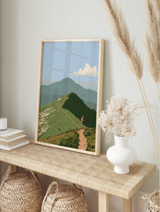 Illustrative mountain hiker wall art with a dirt trail on a grassy ridge and a distant peak, in an alternate framed mockup