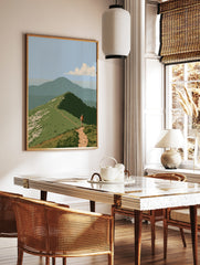 Illustrative mountain hiker wall art with a dirt trail on a grassy ridge and a distant peak under a, in a styled room mockup