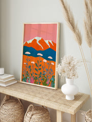 Stylised mountain landscape art print with orange peaks, white snow, blue lake, and white, in an alternate framed mockup