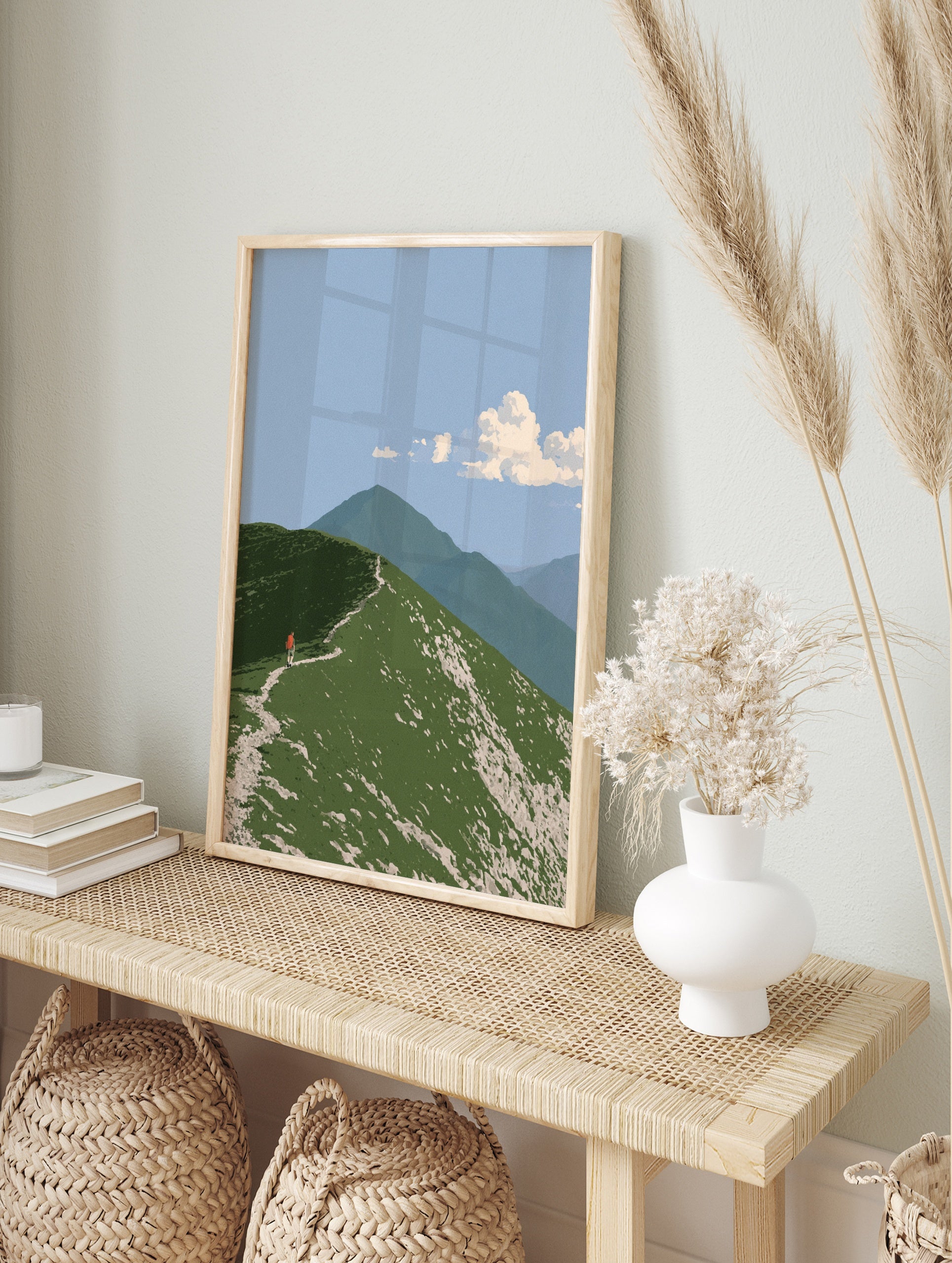 Illustrative mountain ridge wall art with a hiker wearing a red backpack on a green grassy, in an alternate framed mockup