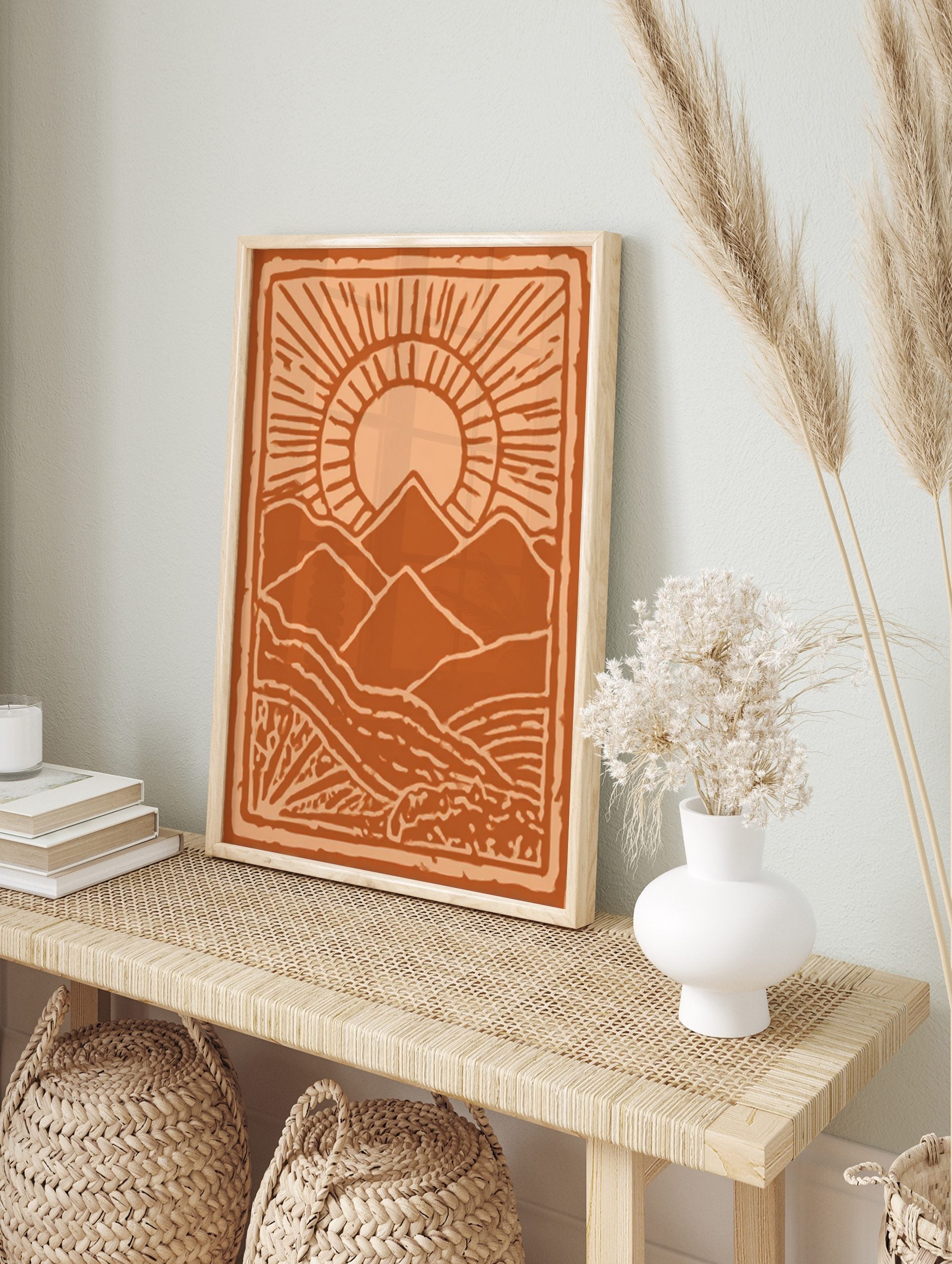 Stylised orange mountain landscape art print with a radiant sun and textured foreground, in an alternate framed mockup