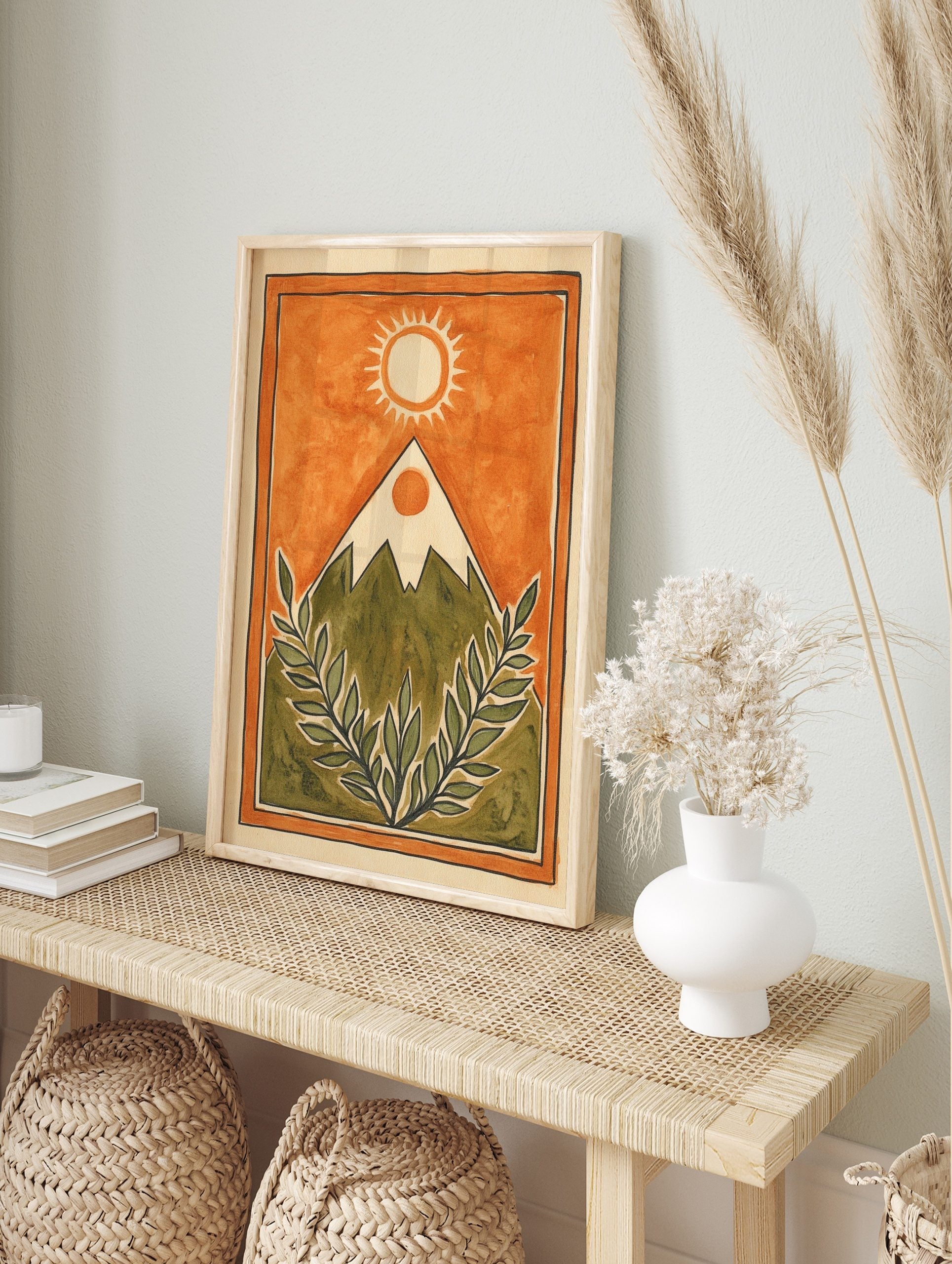 Illustrative mountain landscape with sun and green leafy branches on an orange background, in an alternate framed mockup