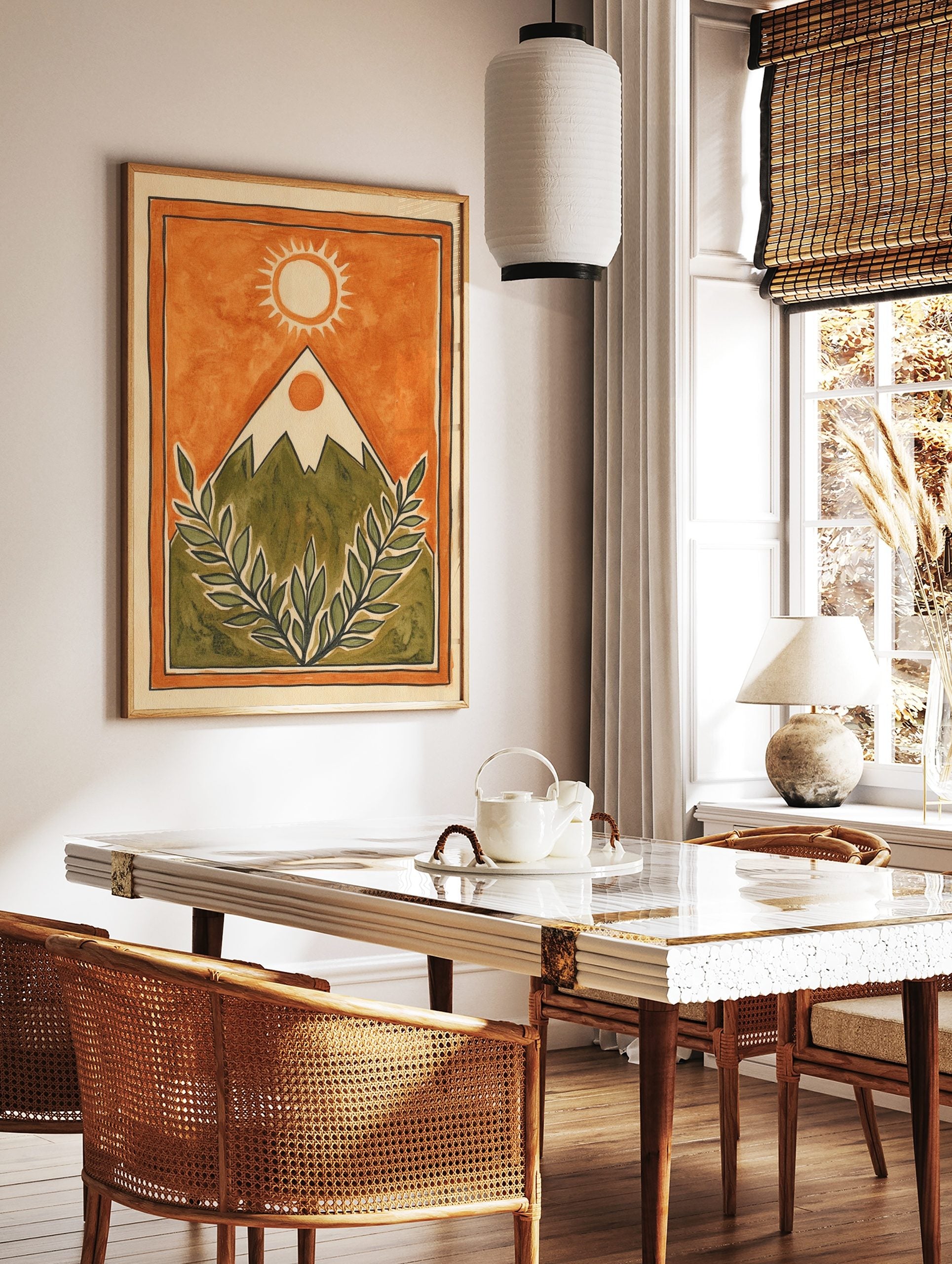 Illustrative mountain landscape with sun and green leafy branches on an orange background, framed, in a styled room mockup