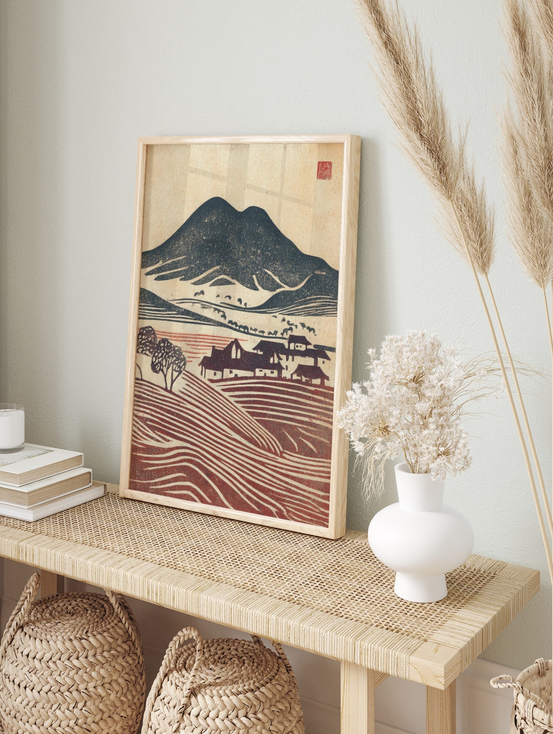 Woodblock print of navy mountains, red terraced fields, and houses in a rustic village, in an alternate framed mockup