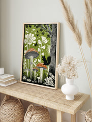 Illustrative green forest print with black squirrel on spotted mushroom and white plants, in an alternate framed mockup