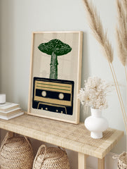 Linocut style illustration of a green mushroom growing out of a dark blue cassette tape on a, in an alternate framed mockup
