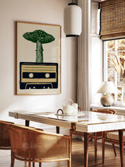 Linocut style illustration of a green mushroom growing out of a dark blue cassette tape on a tan, in a styled room mockup