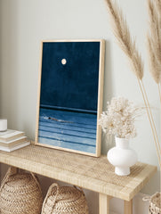 Minimalist art print of a person swimming in dark blue water under a full moon at night, in an alternate framed mockup