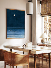 Minimalist art print of a person swimming in dark blue water under a full moon at night, in a styled room mockup