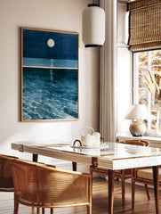 Illustrative wall art of a solitary figure swimming in deep blue ocean water under a full moon with, in a styled room mockup