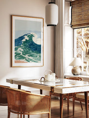 Illustrative ocean wave art print with blue and green water, white foam, and light blue sky over a, in a styled room mockup