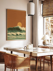 Illustrative ocean waves with white foam crests and a large orange setting sun against an earthy sky, in a styled room mockup